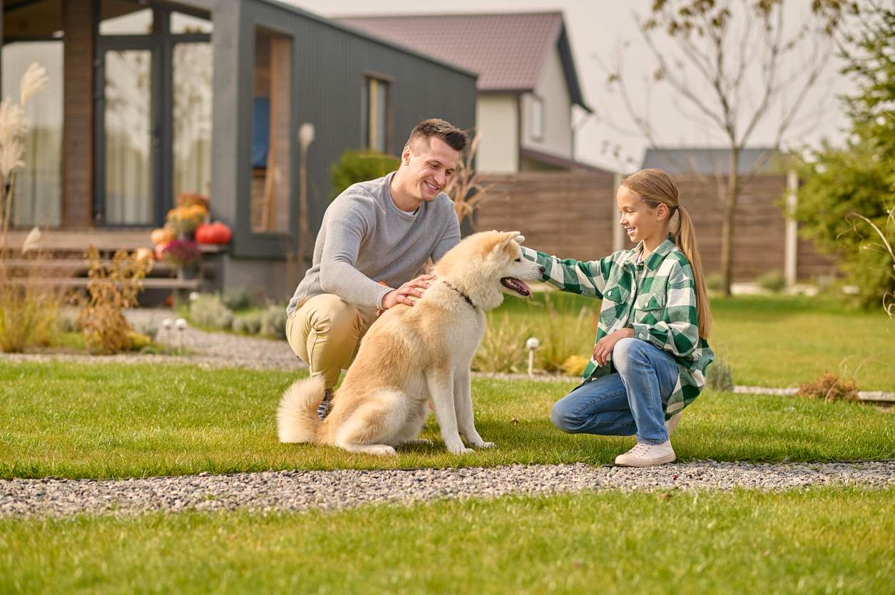 Father and daughter petting their dog in their yard.