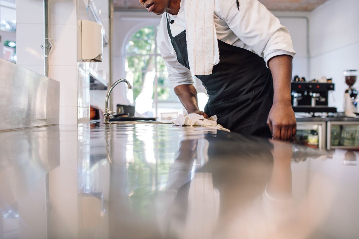 A homeowner wiping down their kitchen counter to clean and prevent pests.