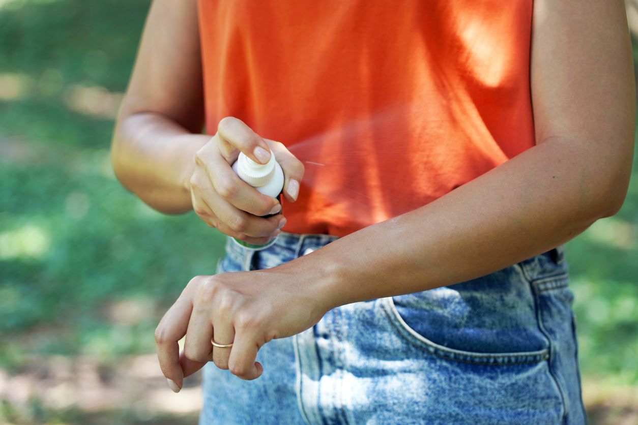 A woman applies bug spray to her arm while outdoors.