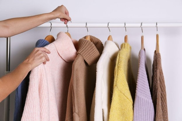 Sweaters hanging on a clothes rack, with a person taking one sweater and hanger off the rack.