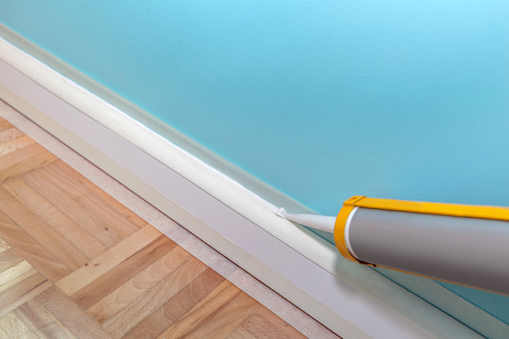 Alt text: An image of caulk being applied to a baseboard