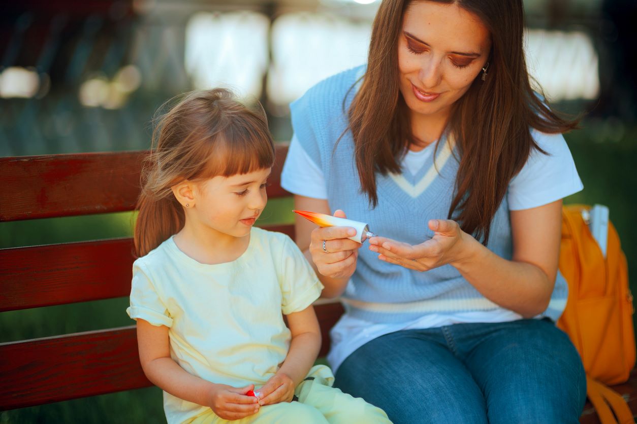 A mother and daughter applying skin cream on a park bench.