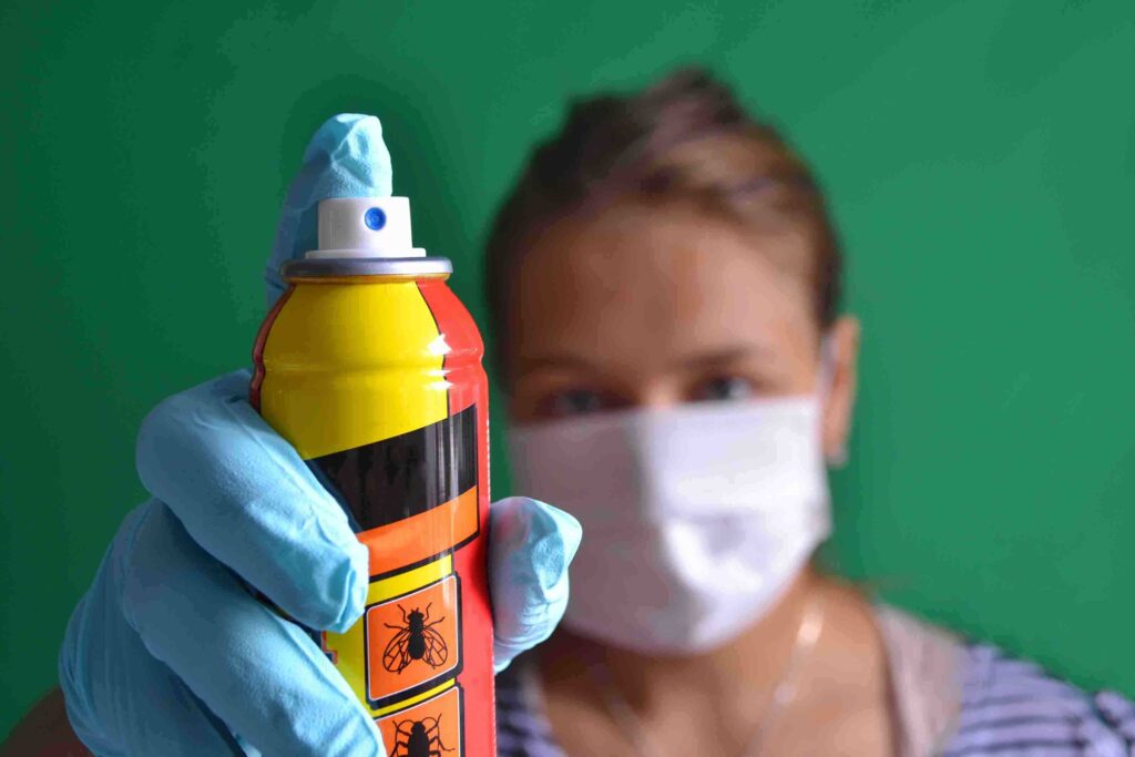 Aerosol for insect control in the hands of a woman wearing a mask.