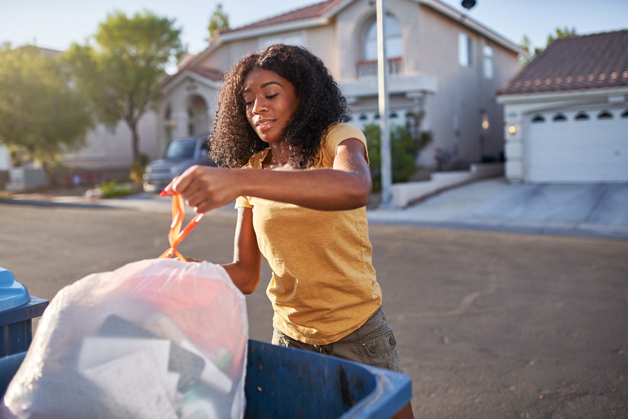 A woman takes out the trash to a curbside bin right outside her house.