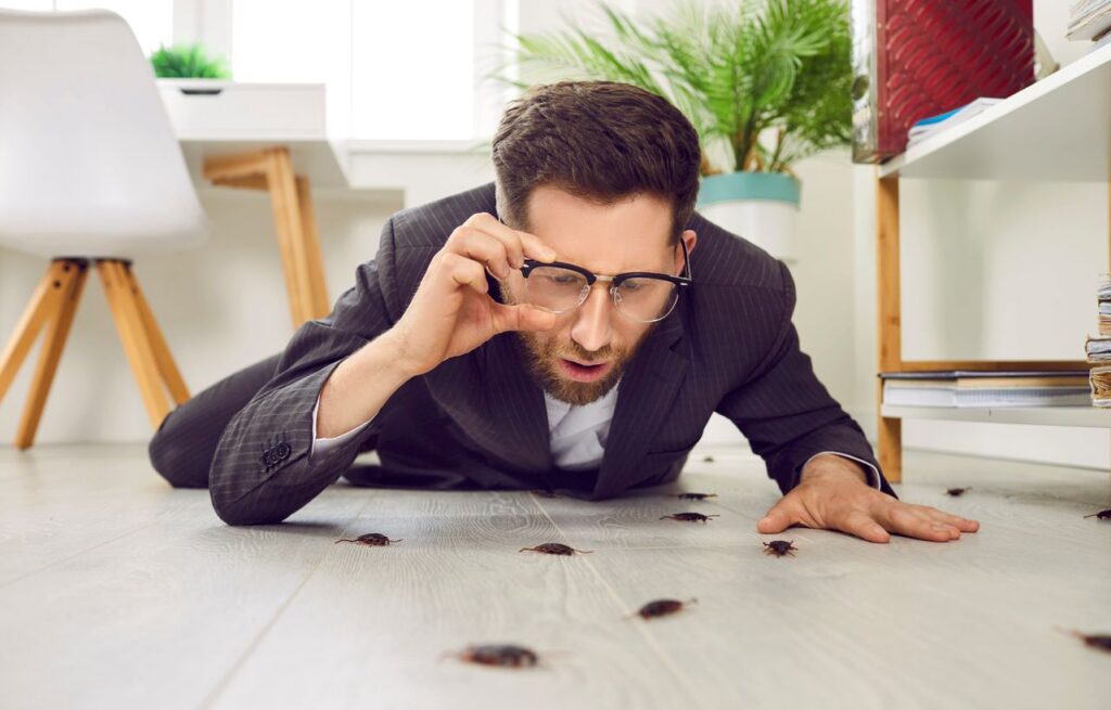 A man humorously raises his glasses to look at a sudden influx of cockroaches in his home.