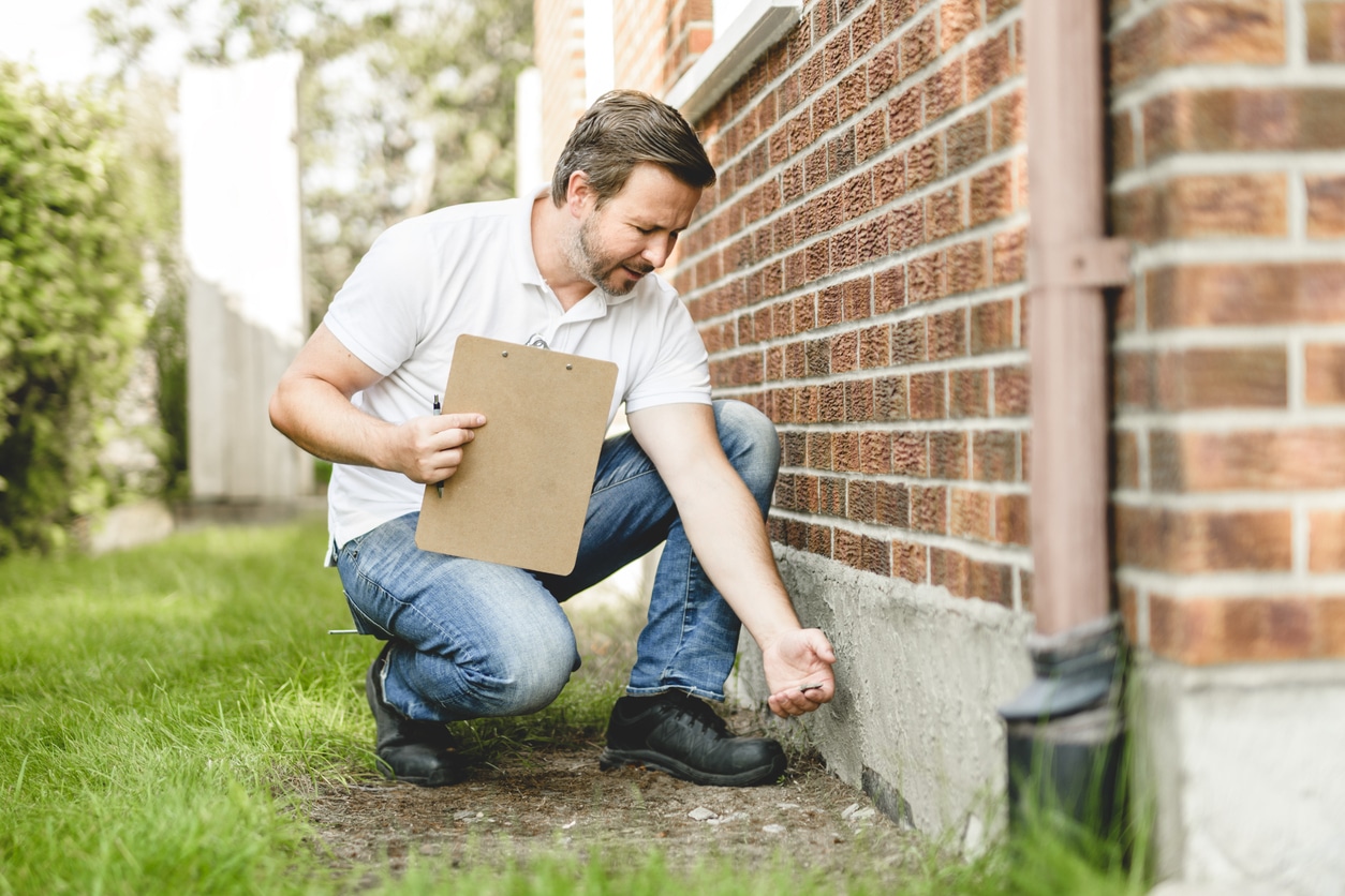 Pest control technician inspecting the foundation along the exterior of a brick building.