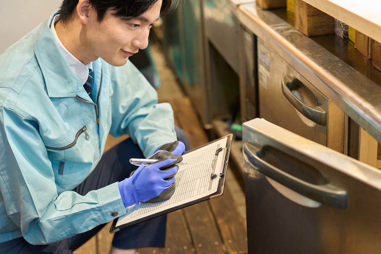 Pest control technician documenting an inspection inside a commercial kitchen.
